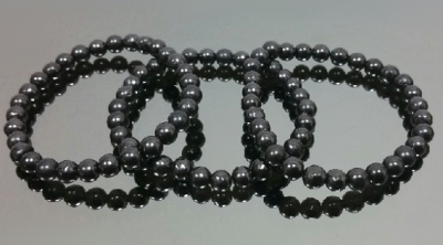 Quatro pulseiras de contas negras brilhantes em superfície cinza refletora