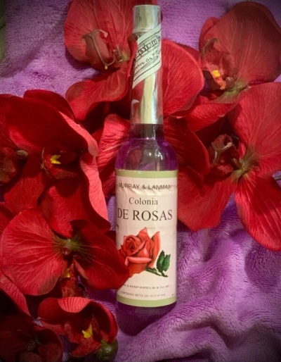 Frasco de colónia de rosas rodeado por pétalas vermelhas sobre pano lilás