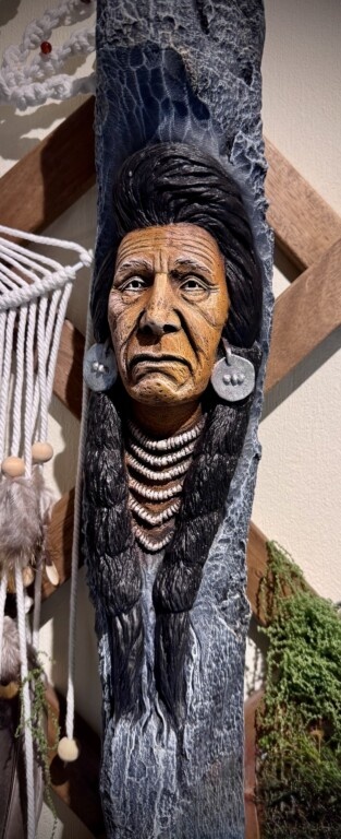 Escultura de rosto indígena detalhado em madeira com colares e brincos grandes