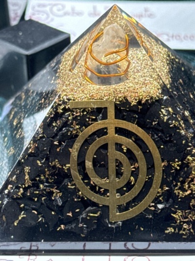 Pirâmide decorativa com símbolo geométrico dourado e elementos dentro de resina transparente