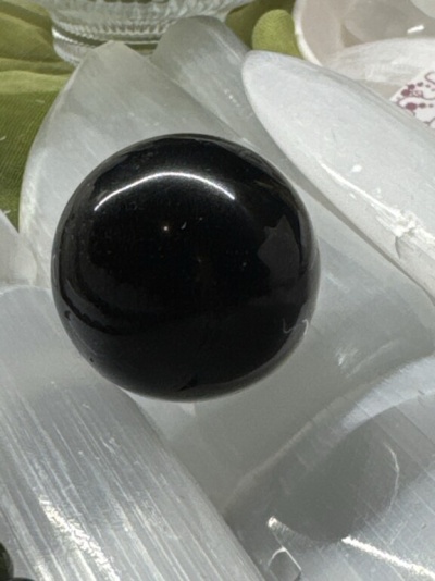 Esfera preta brilhante sobre lâminas claras em fundo com tecido verde e prato branco