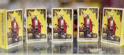 Cinco baralhos de tarot Rider Waite alinhados sobre superfície espelhada com a carta O MAGO na frente.