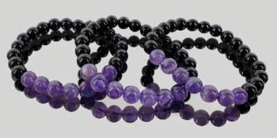 Três pulseiras de contas pretas e roxas em fundo cinza claro