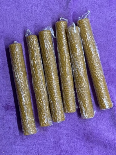 Seis velas de cera de abelha enroladas em padrão de favo hexagonal sobre tecido roxo.