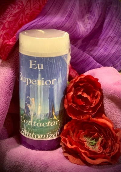 Vela branca com rótulo azul e texto em português rodeada por toalhas e flores vermelhas.
