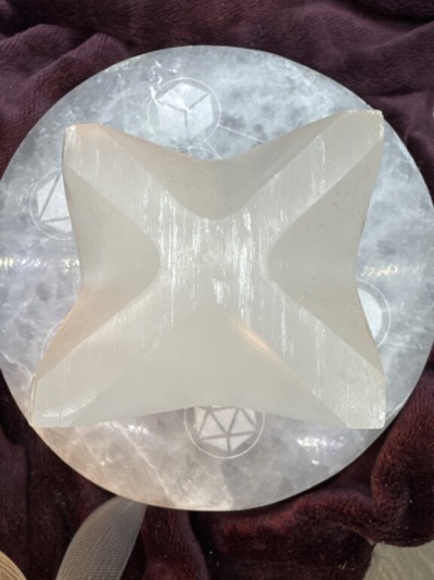 Escultura geométrica em cristal branco sobre base circular com símbolos, em fundo de tecido bordô