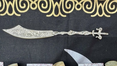 Navalha metálica decorativa com cabo e lâmina gravados sobre tecido preto com padrão amarelo