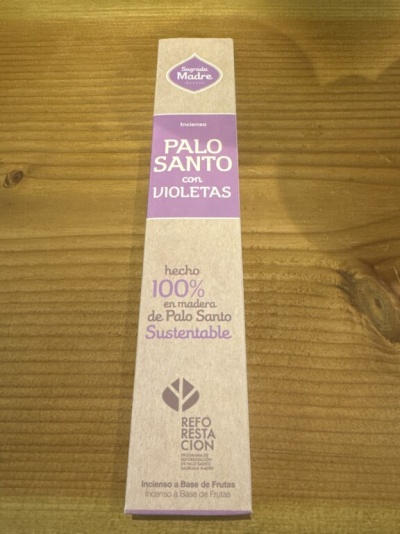 Embalagem de incenso Palo Santo com violetas em embalagem de papel reciclado sobre mesa de madeira clara