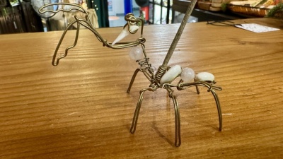 Escultura de insecto em arame dourado com bolas brancas e transparente numa mesa de madeira