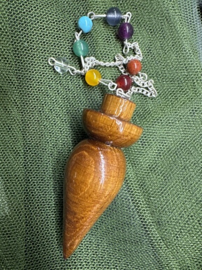 Pingente de madeira com corrente e contas coloridas sobre tecido verde
