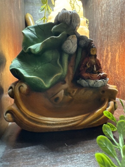 Escultura decorativa com figura sentada e folhas verdes em base castanha