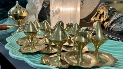Incensários de latão dourado sobre prato verde água com estátua de Ganesha ao fundo