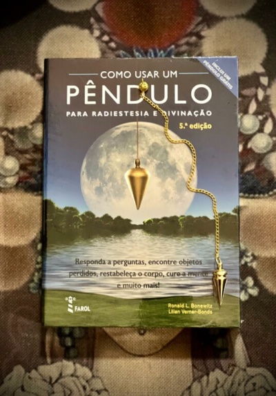 Livro sobre radiestesia com pêndulo dourado posicionado em cima.