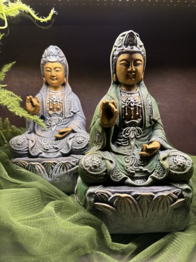 Duas estátuas ornamentadas de figura sentada, verde e cinza, com tecido verde