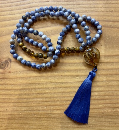 Colar ou pulseira de contas azuis, marrons com pendente redondo e tassel azul sobre madeira