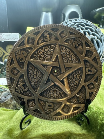 Placa decorativa metálica com pentagrama e símbolos em suporte preto sobre tecido verde
