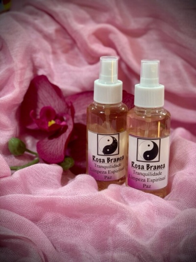 Dois frascos de spray com rótulos Rosa Branca sobre tecido rosa e uma flor