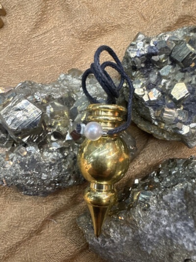 Pingente dourado com cordão preto sobre pedras metálicas