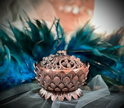 Incensário de metal cobre com padrão de pétalas e tampa decorativa em tecido de tule cinza e penas azuis