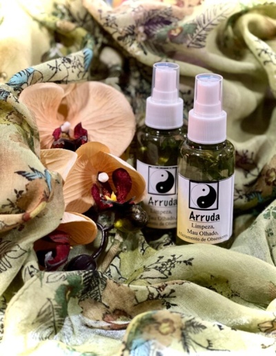 Duas garrafas de spray Arruda sobre tecido floral com flores artificiais
