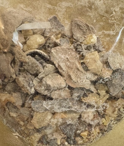 Saco transparente com pedaços irregulares de mineral ou resina natural em cores castanhas, amarelas e pretas