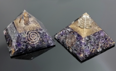 Duas pirâmides de orgonite com detalhes em cobre e base roxa sobre superfície preta