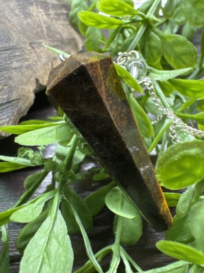 Pêndulo de cristal marrom facetado com corrente azul entre folhas verdes e madeira.