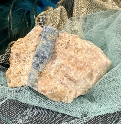 Roca mineral rosada com faixa cinzento-azulada sobre tecido de malha verde e dourado.