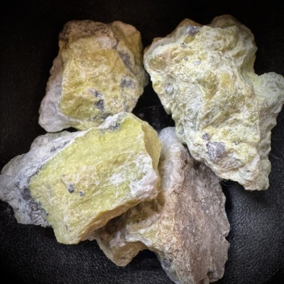 Pedras minerais amareladas e brancas com textura rugosa sobre fundo preto