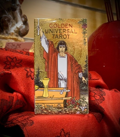 Caixa de tarot GOLDEN UNIVERSAL TAROT com figura de pessoa vestindo vermelho sobre tecido vermelho.