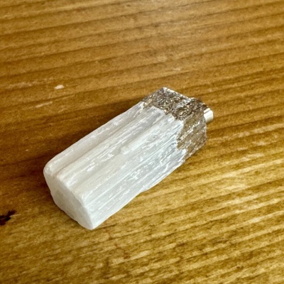 Pingente de cristal branco com topo metálico prateado sobre madeira