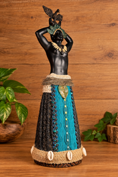 Estatueta decorativa masculina com adereços coloridos e saia de tecido sobre fundo de madeira.
