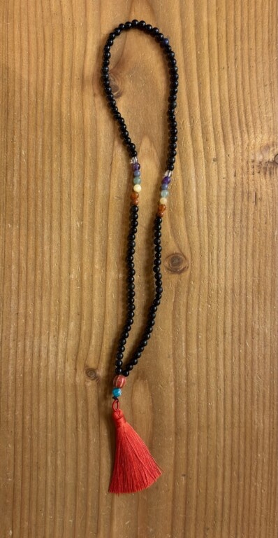 Colar de contas pretas com contas coloridas e tassel vermelho em fundo de madeira.