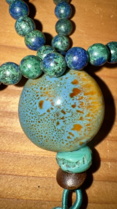 Colar com contas em tons de azul, verde e castanho sobre mesa de madeira