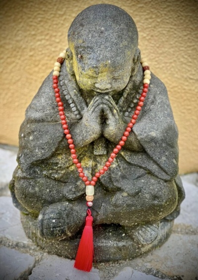 Estátua de monge de pedra com contas vermelhas e bege e borla vermelha