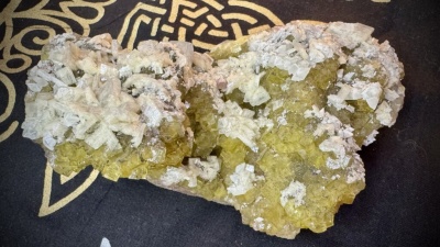 Cristal mineral amarelo com cristais brancos sobre fundo preto com padrão dourado