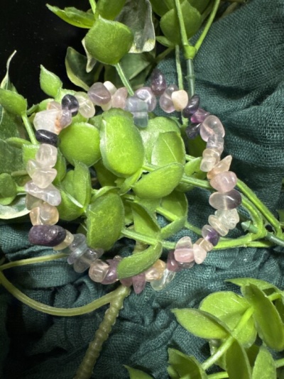 Pulseira de pedras naturais em tons rosa e roxo sobre folhagem verde e tecido escuro