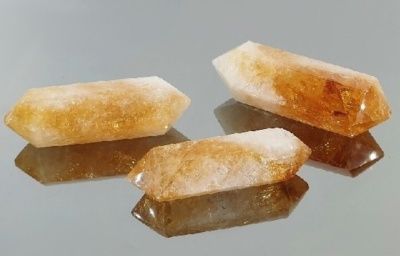 Três cristais de quartzo citrino amarelo e branco sobre superfície espelhada cinzenta