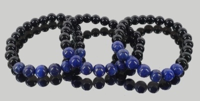 Três pulseiras de contas pretas e azuis refletidas numa superfície clara