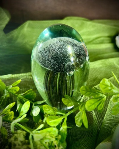 Objeto decorativo em vidro com padrão preto e branco sobre tecido verde e folhas verdes