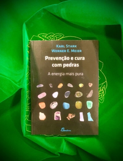 Livro sobre prevenção e cura com pedras sobre tecido verde bordado.