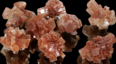Cristais naturais de aragonite castanho e laranja em formas hexagonais sobre fundo preto