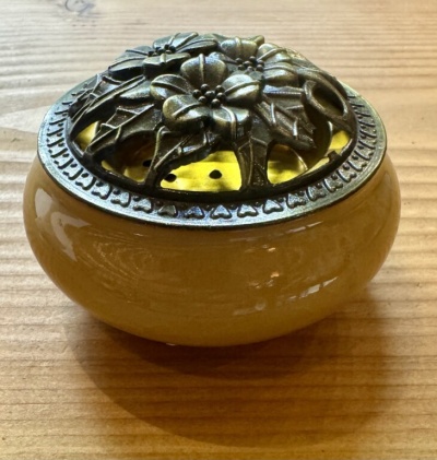 Vaso redondo amarelo com tampa metálica decorativa floral sobre mesa de madeira