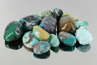 Pedras semipreciosas polidas em tons de verde, azul e castanho sobre fundo cinzento