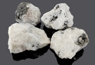 Quatro pedras minerais brancas com manchas pretas sobre fundo preto
