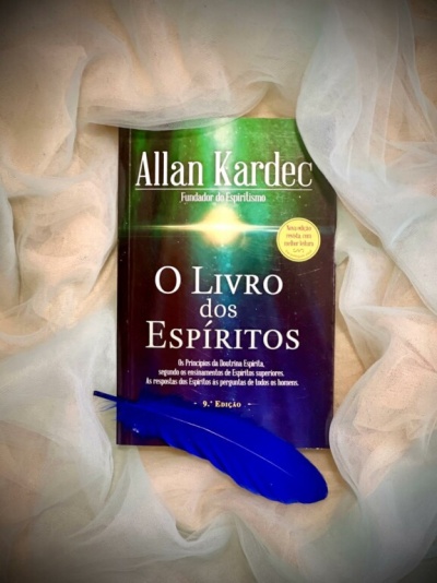 Livro O Livro dos Espíritos junto a tecido branco e pena azul