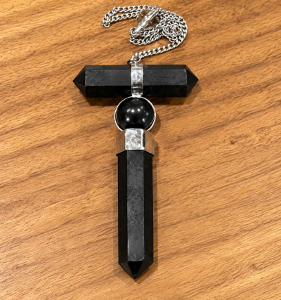 Colar com pendente em forma de cruz em pedra negra e metal prateado sobre madeira clara