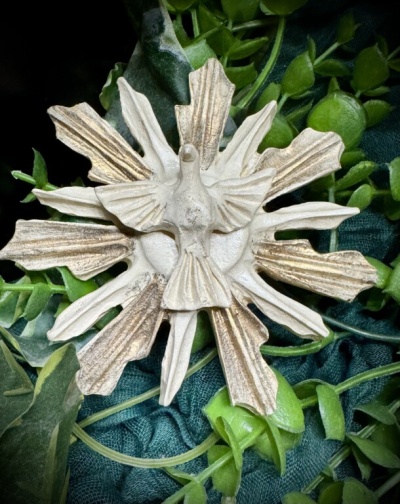 Adorno decorativo branco e dourado com forma de sol e pássaro sobre tecido verde e folhas