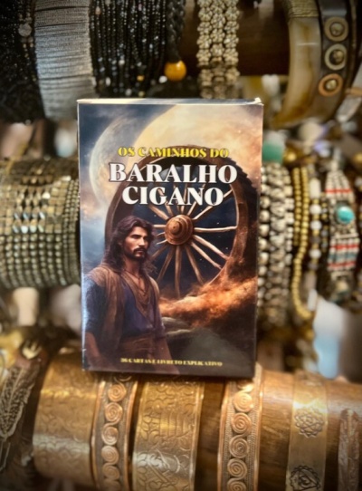 Caixa de baralho cigano com ilustração e texto em português em cima de braceletes decorativos.