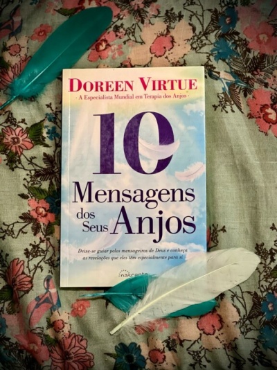 Livro 10 Mensagens dos Seus Anjos sobre tecido floral com três penas ao redor